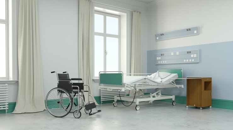 Leeres Krankenzimmer mit Bett und Rollstuhl im Pflegeheim