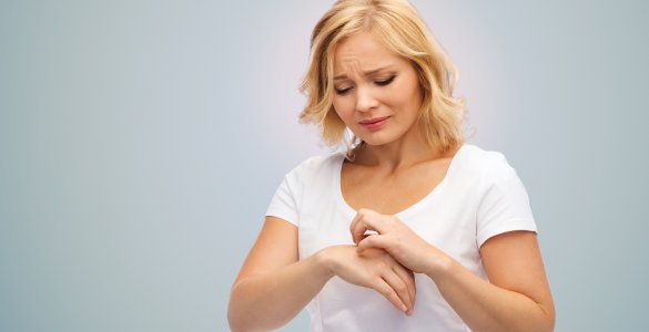 Frau kratzt sich an der Hand.