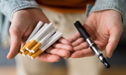 Person hält Zigaretten und E-Zigarette in der Hand